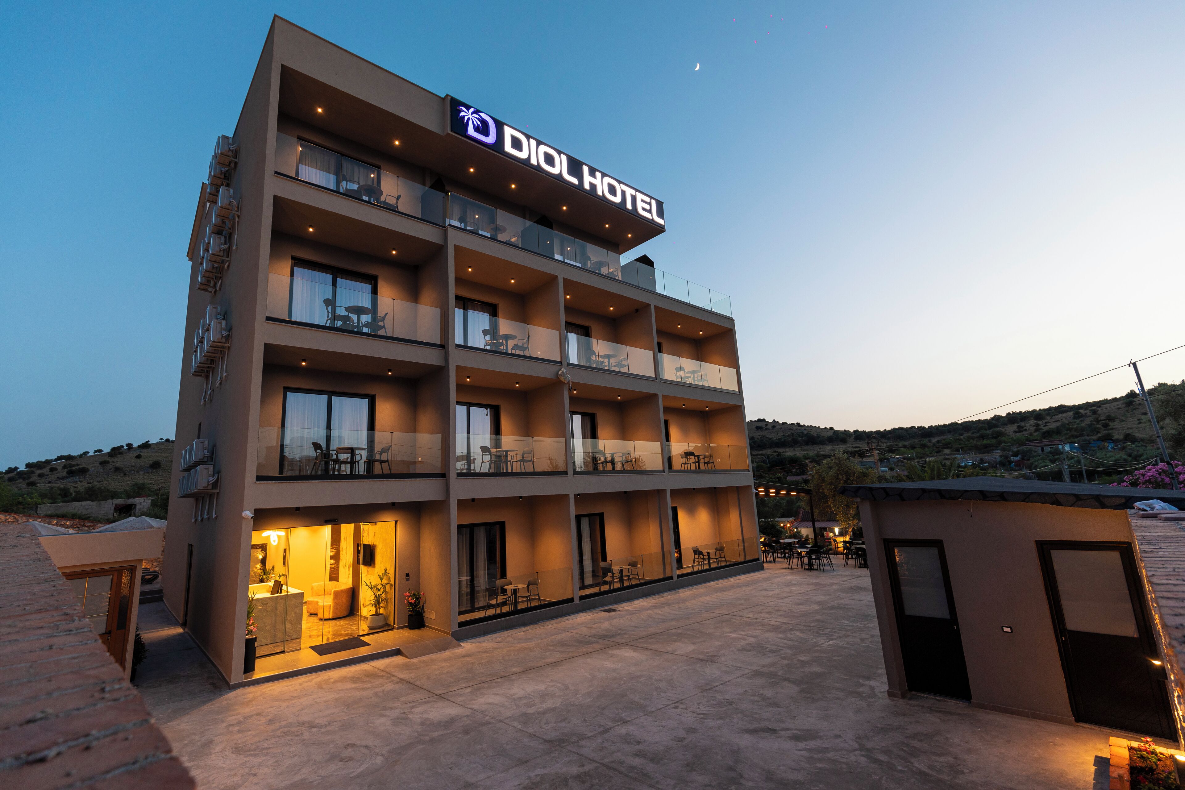 Un hotel moderno con varios balcones, una entrada bien iluminada y una vista despejada del paisaje circundante.