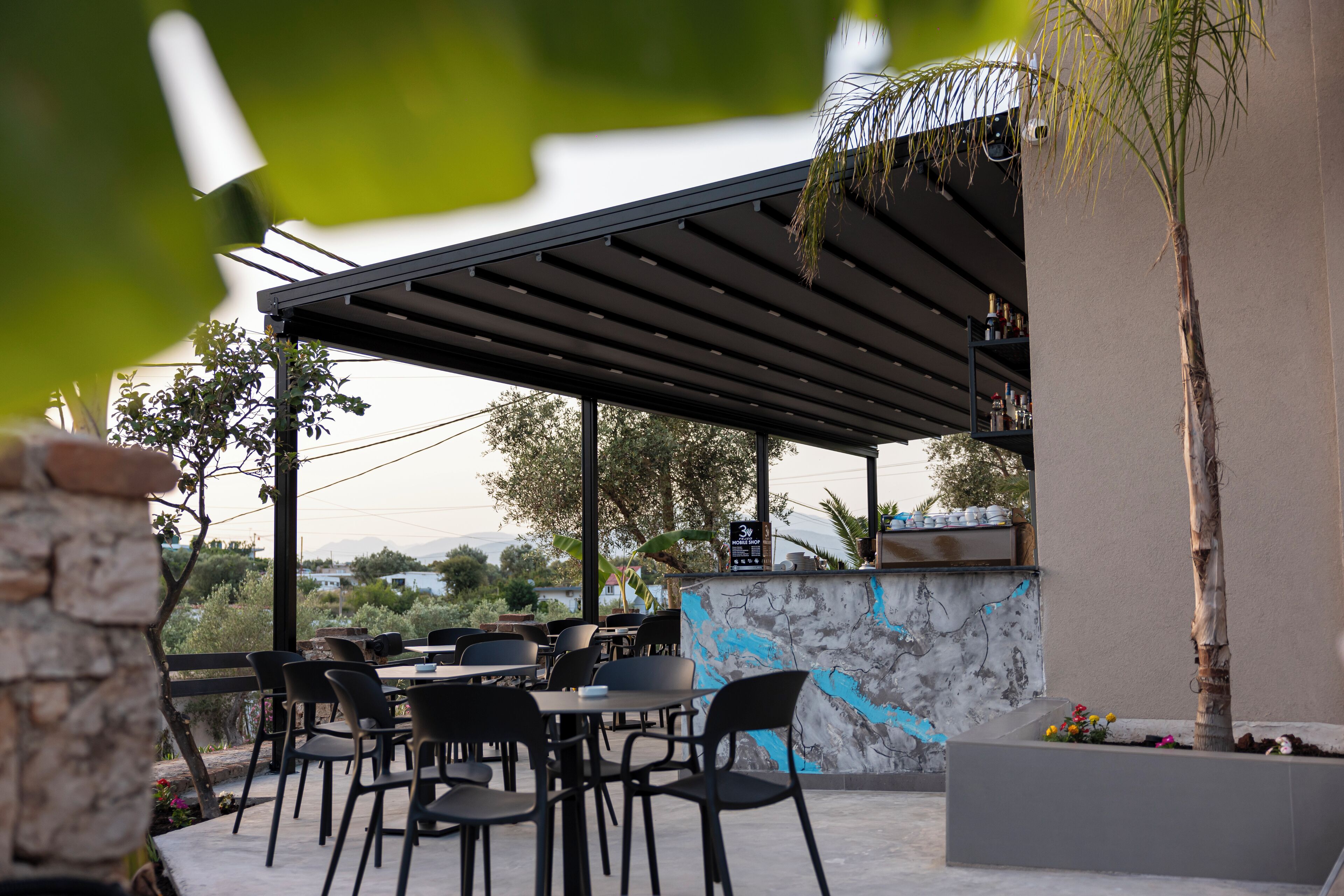 An outdoor patio with tables and chairs, a stone wall with a mural, and a bar area with shelves.