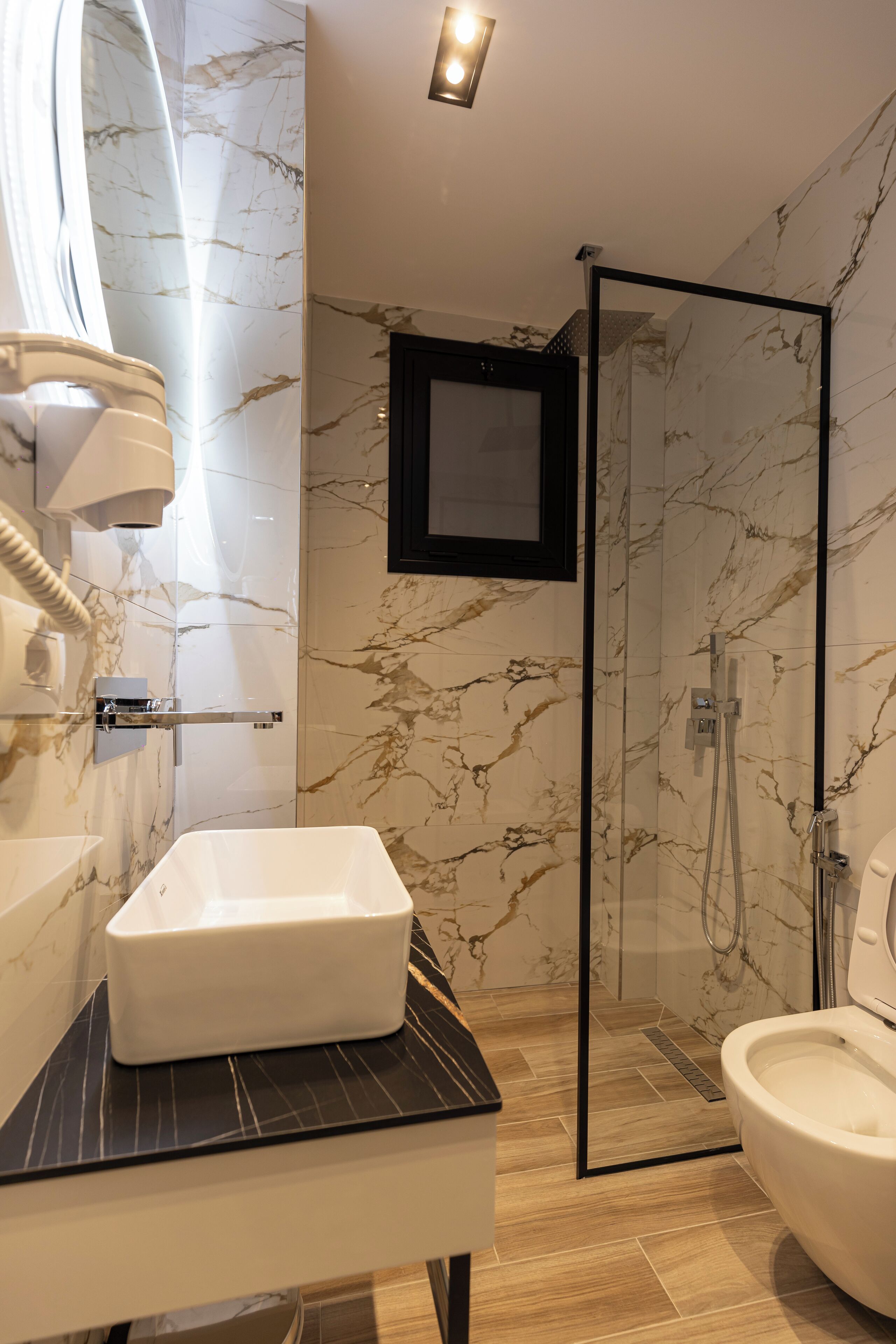 A modern bathroom with a marble backsplash, a glass-enclosed shower, a white sink, and a toilet.