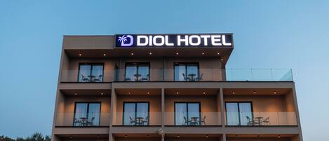 A modern hotel building with a sign reading "DIOL HOTEL". It features multiple balconies with outdoor seating and large windows.