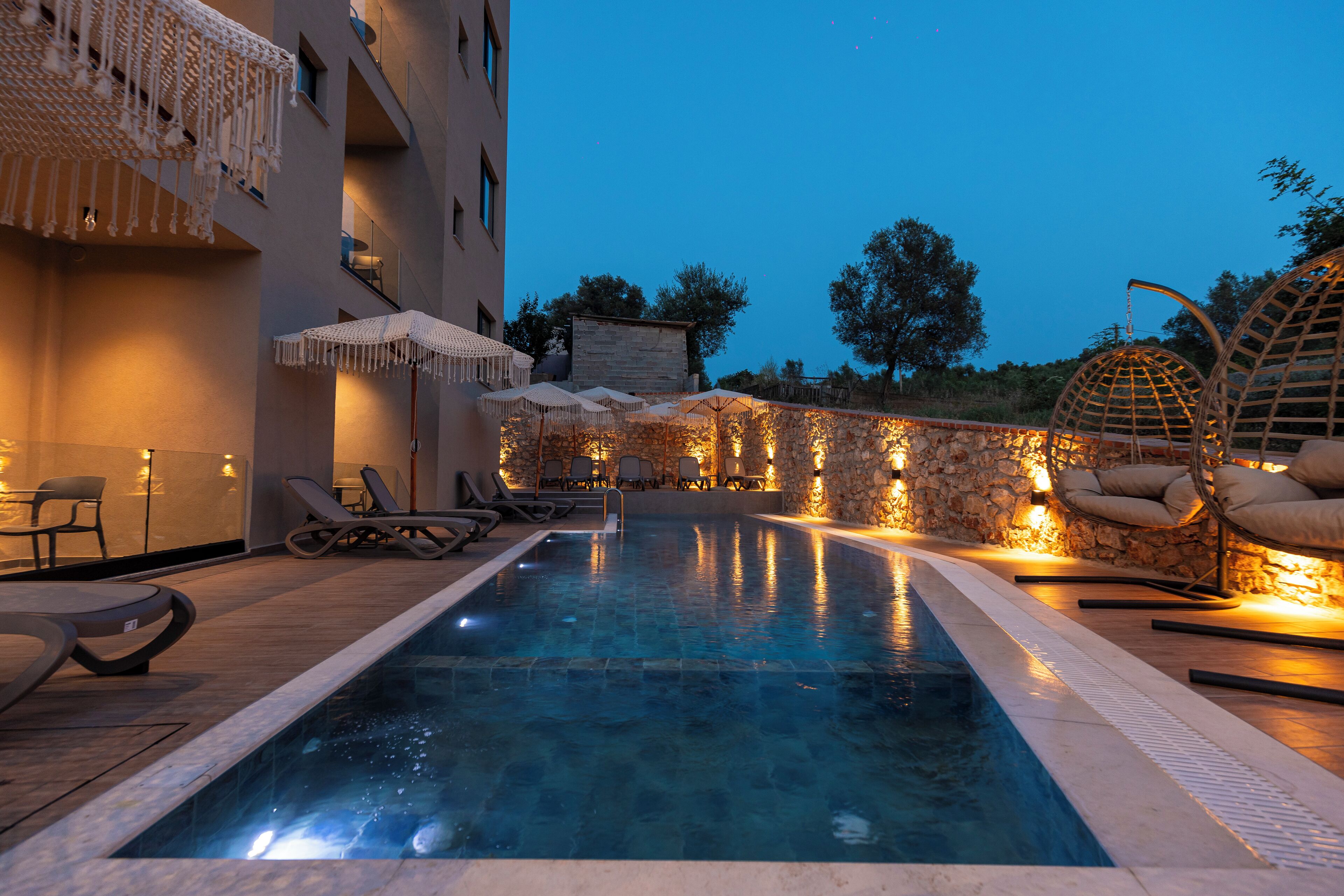 A swimming pool with lounge chairs and umbrellas, surrounded by stone walls and warm lighting.