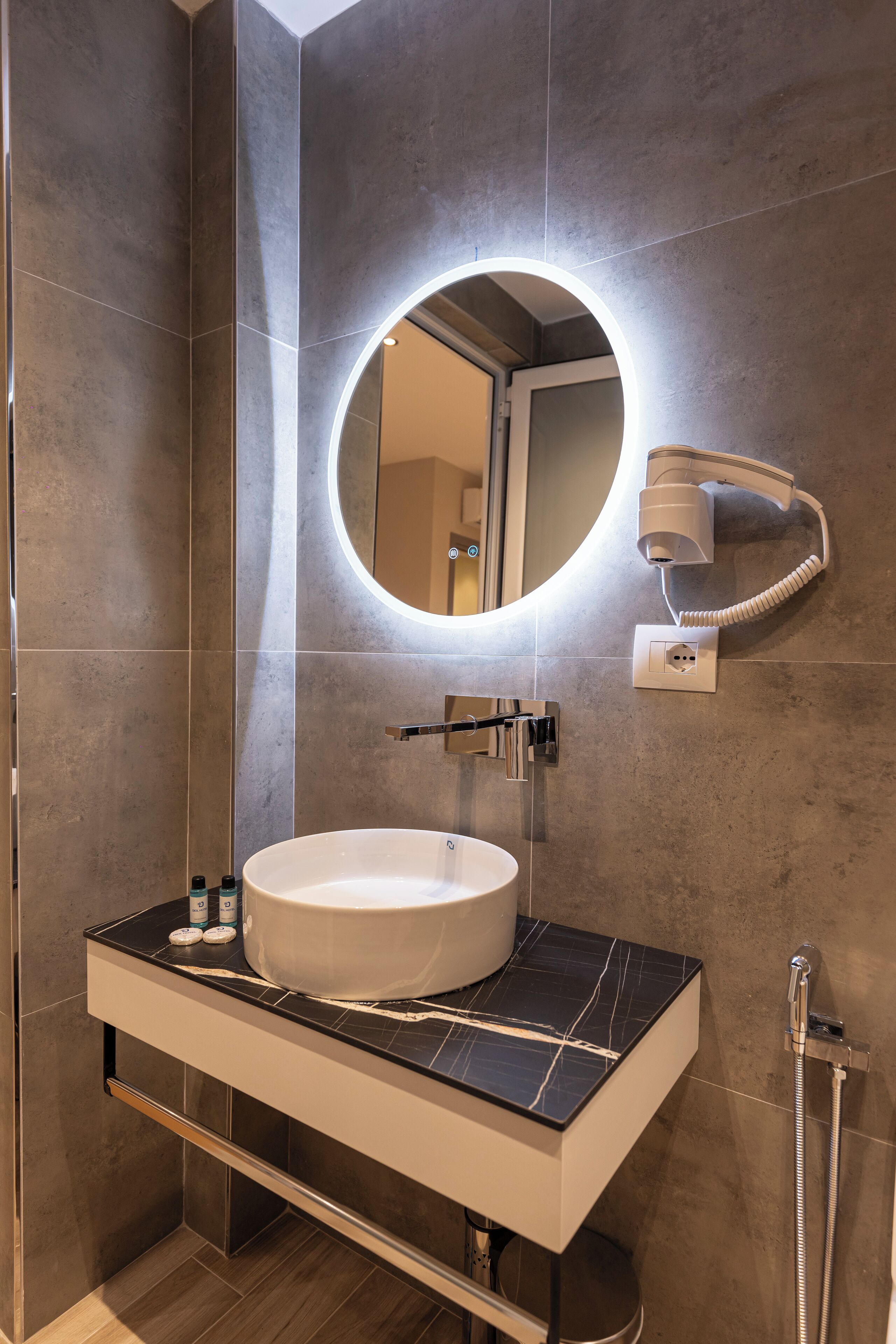 A modern bathroom with a large round mirror, a white sink, and a handheld showerhead.