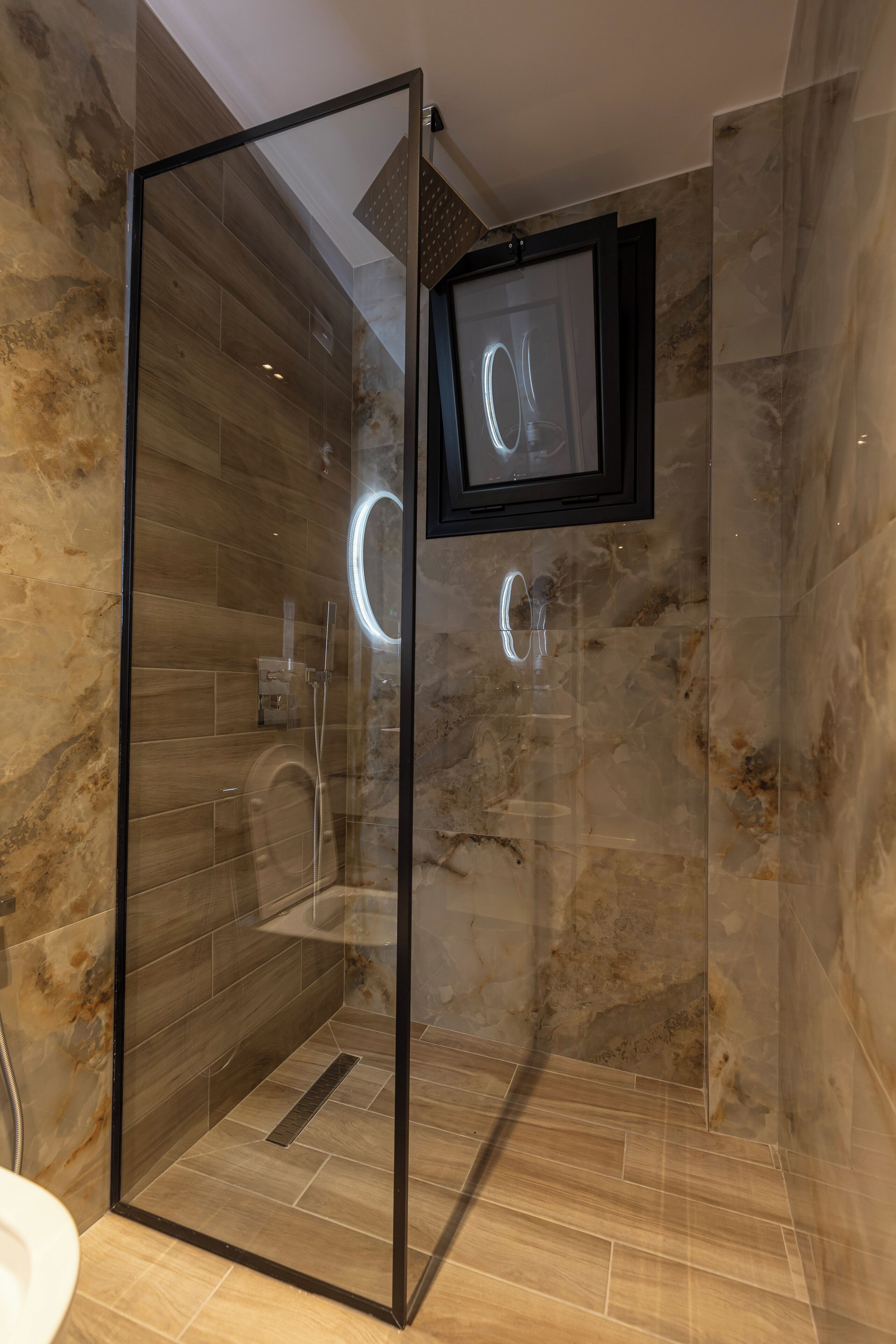 A modern bathroom with a glass-enclosed shower, marble walls, and a mounted TV.