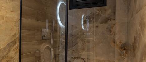 A modern bathroom with a glass-enclosed shower, marble walls, and a mounted TV.