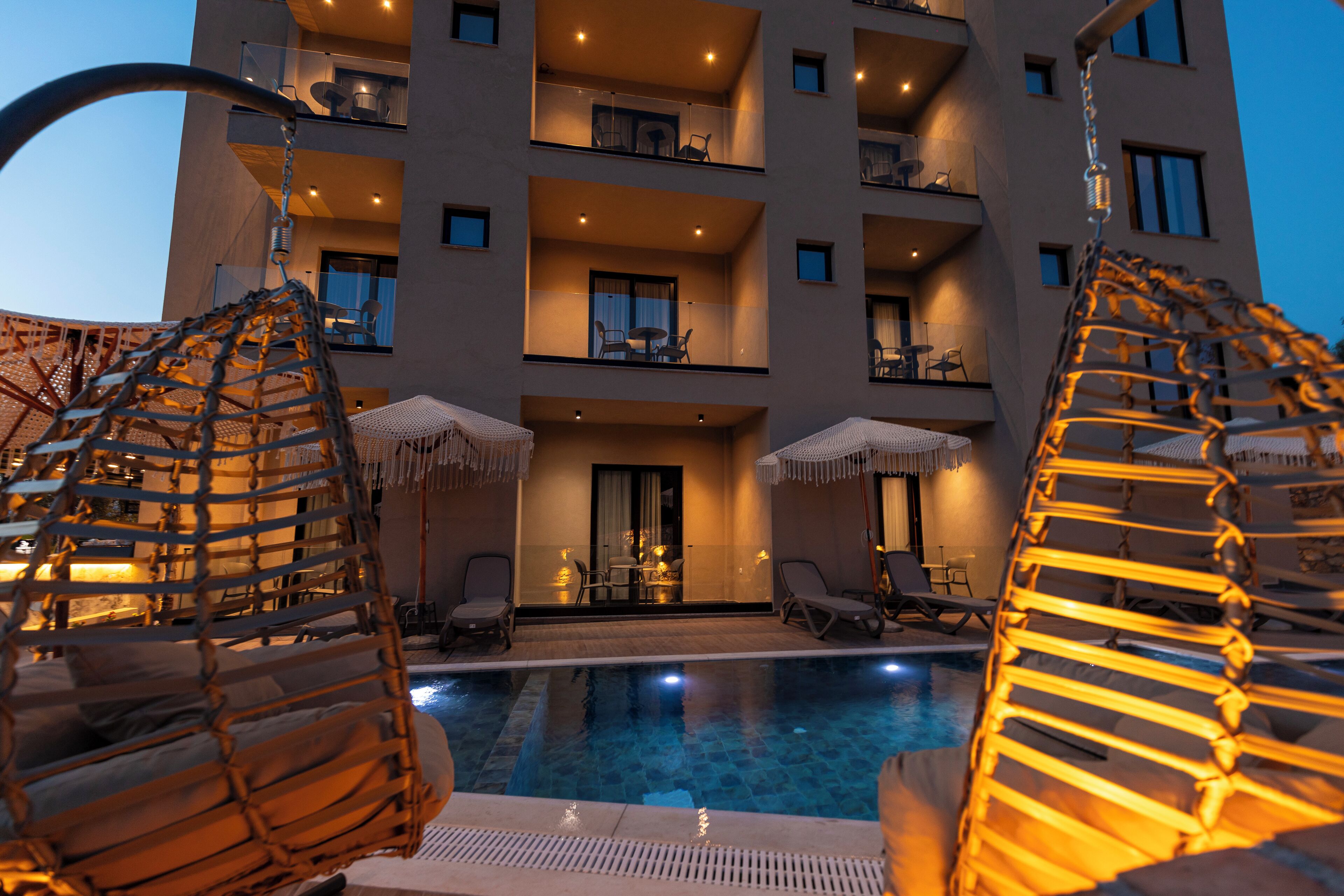 A poolside area with lounge chairs and umbrellas, a pool, and a building with balconies and windows.