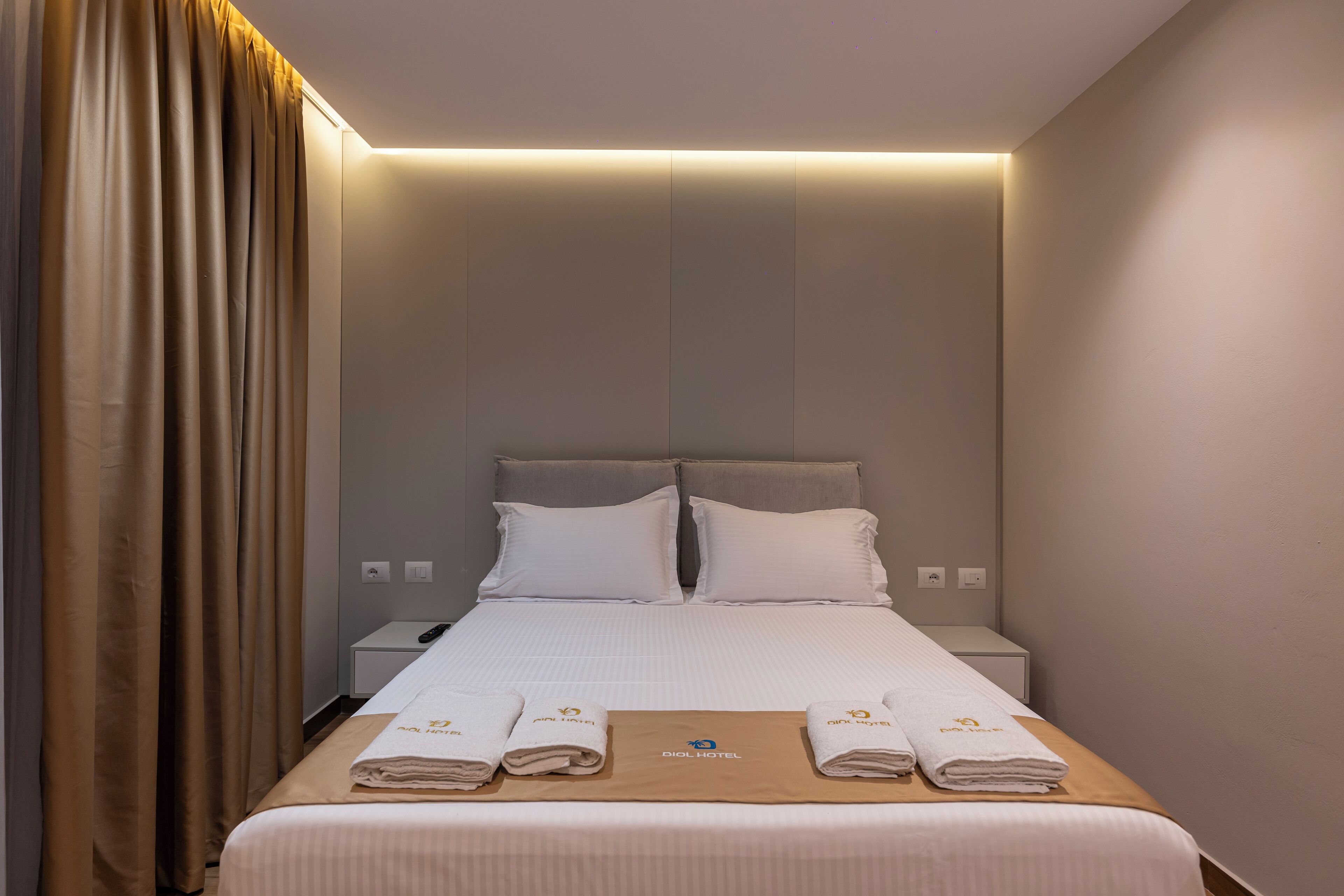 A hotel room with a neatly made bed, two pillows, a bedside table with a lamp, and a wall-mounted light.