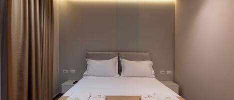 A hotel room with a neatly made bed, two pillows, a bedside table with a lamp, and a wall-mounted light.