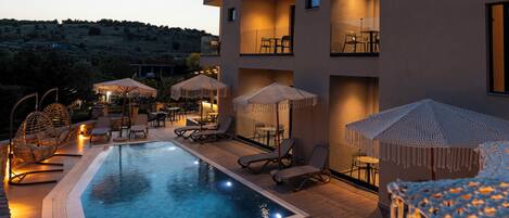 Un hotel moderno con piscina, mobiliario exterior y varios balcones.