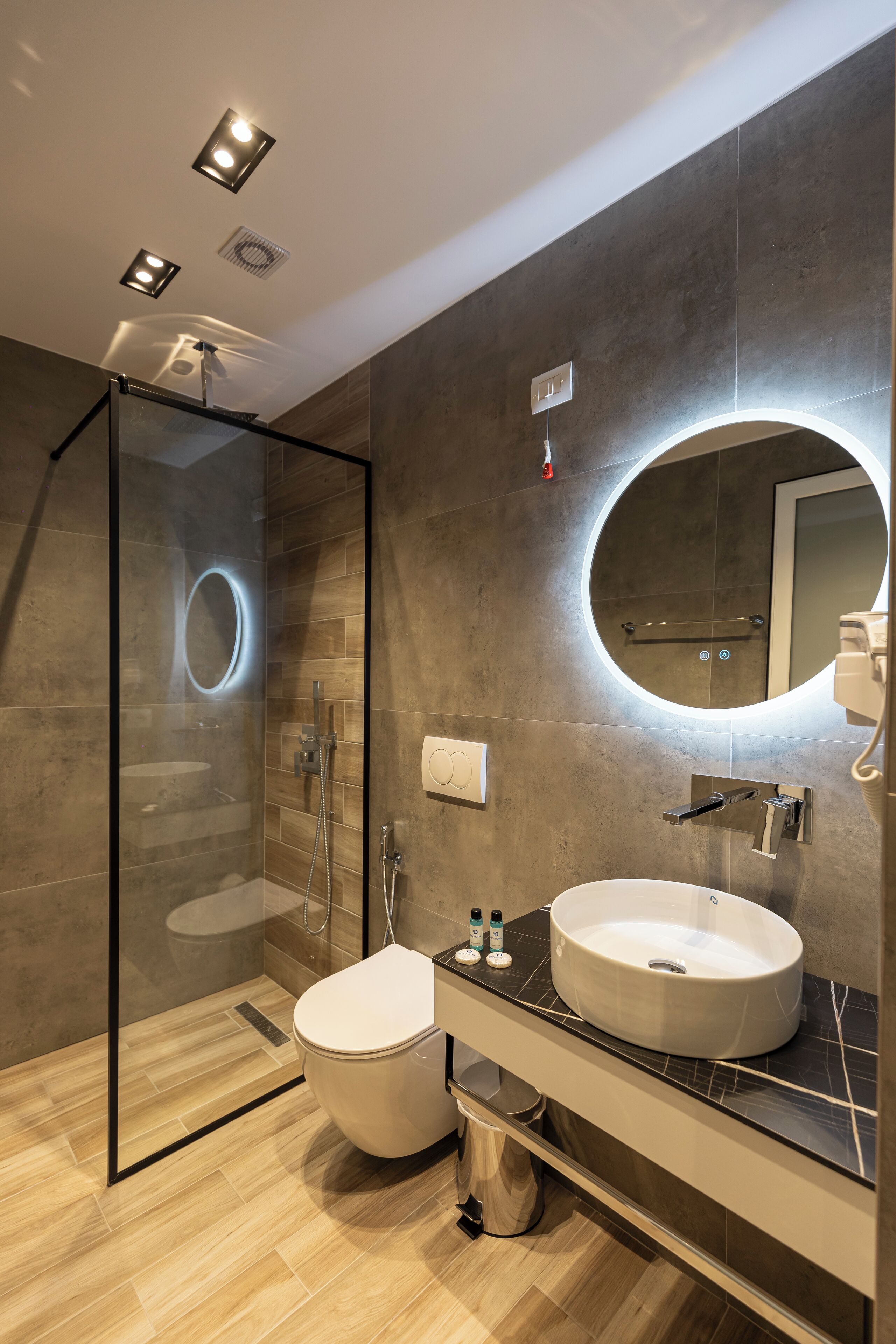 A modern bathroom with a glass-enclosed shower, a round mirror, and a large sink.