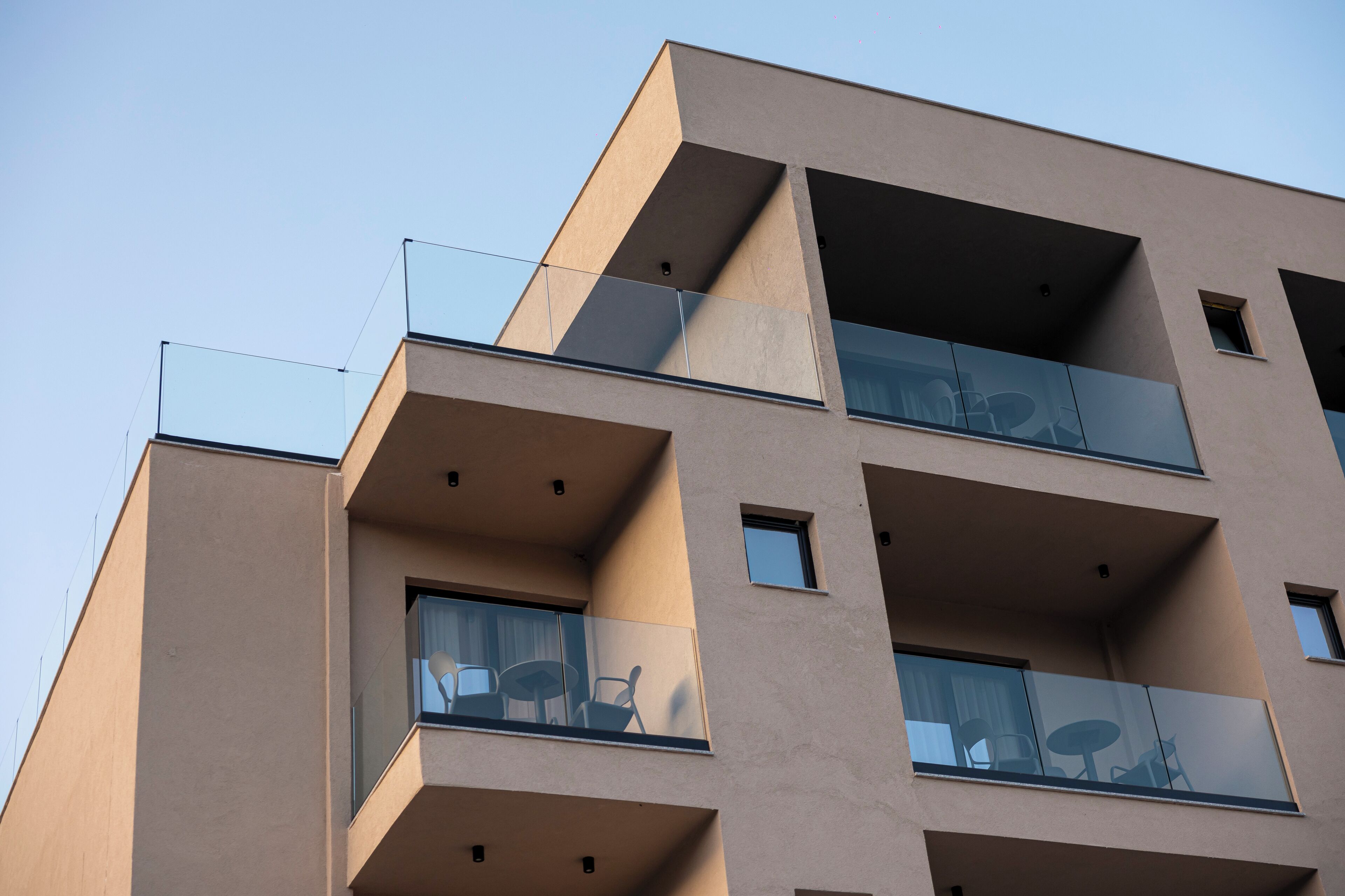 A multi-story building with balconies, large windows, and a clear sky.