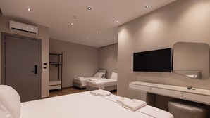 Une chambre d’hôtel avec un grand lit, deux petits lits, un bureau, un miroir et un appareil de climatisation.