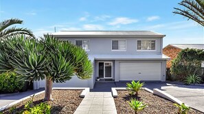 Une maison à deux étages avec un garage, une allée et un petit jardin planté.