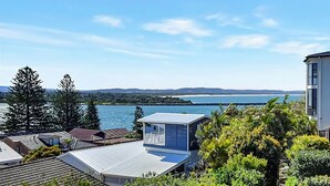A coastal residential area with a view of the sea, houses with sloped roofs, and a small structure with a balcony. - The Sea Serenade - Coastal haven with panoramic ocean views! (Swansea Heads)
