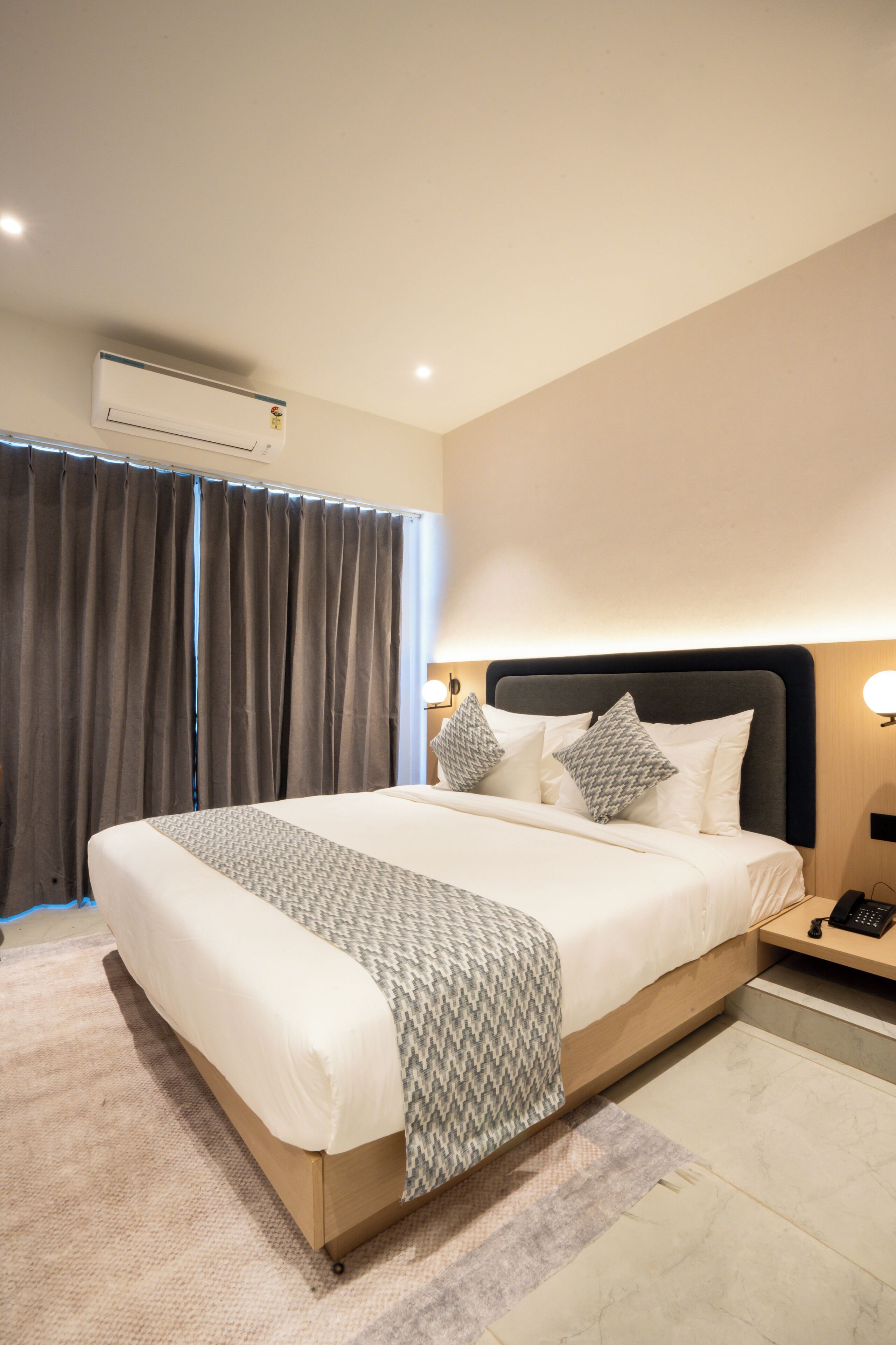 Une chambre d’hôtel moderne avec un grand lit, une table de chevet avec un téléphone et un appareil de climatisation fixé au mur.