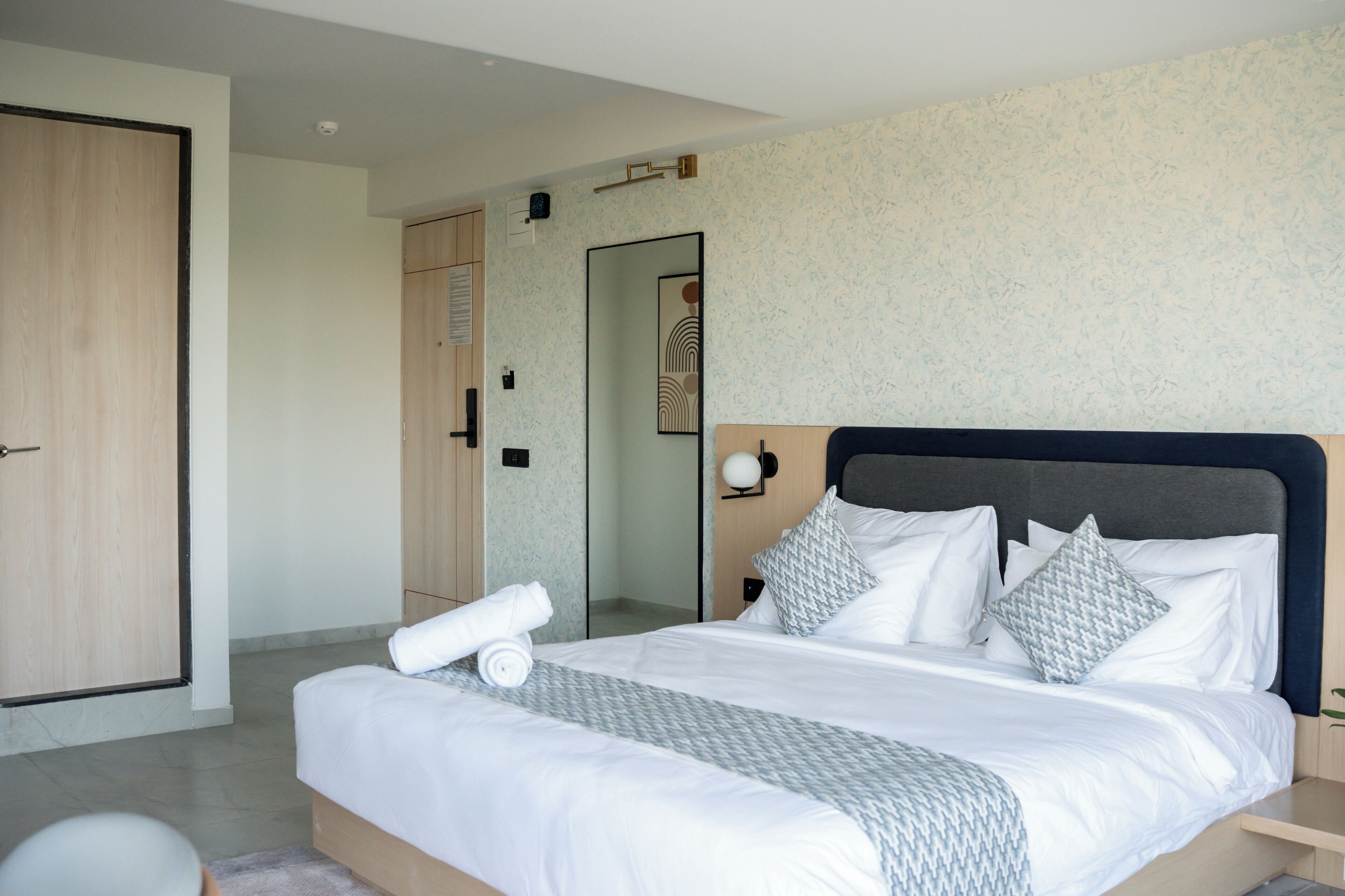 A modern bedroom with a large bed, a wooden wardrobe, and a bathroom visible through an open door.