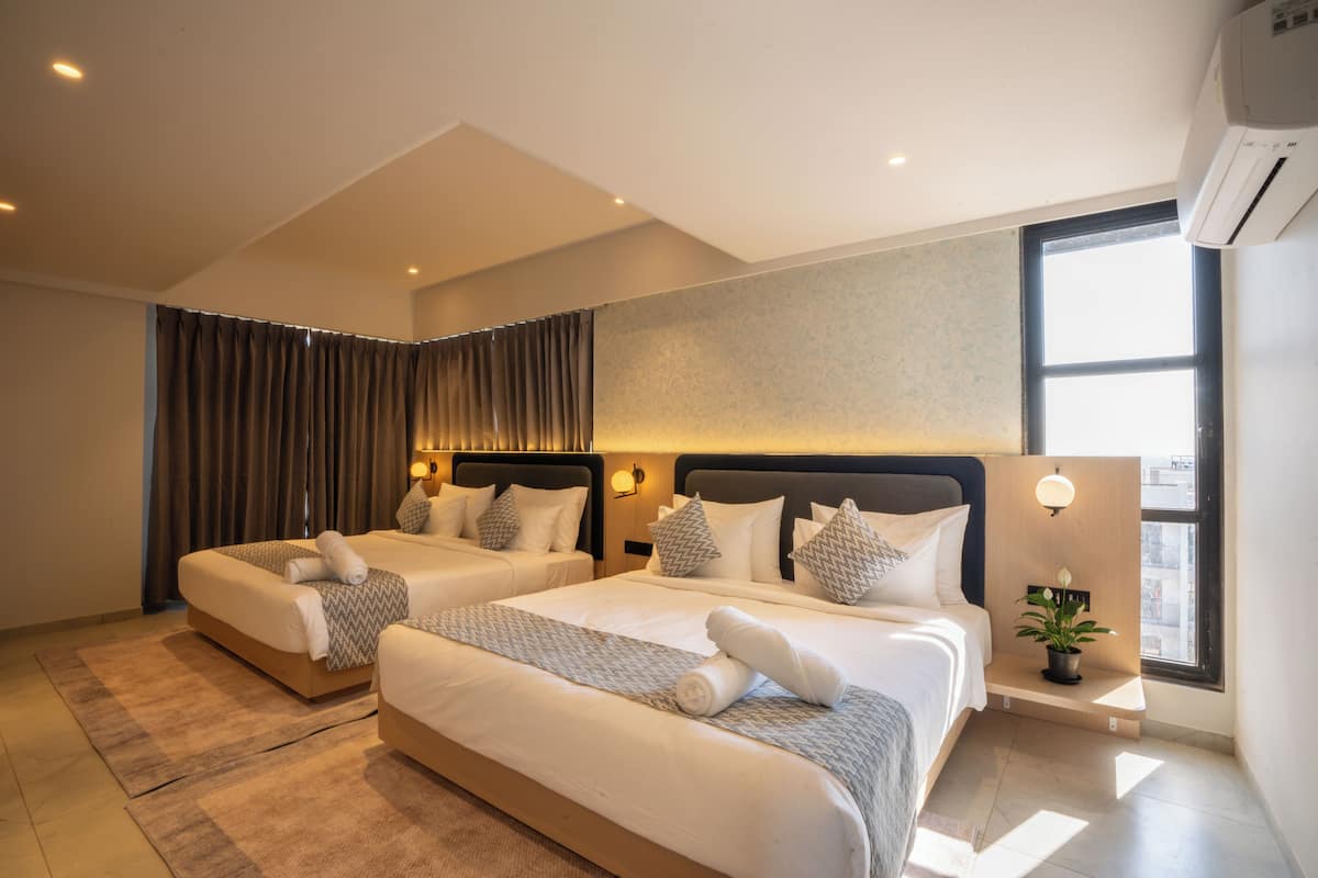 A hotel room with two beds, a large window, and a potted plant.