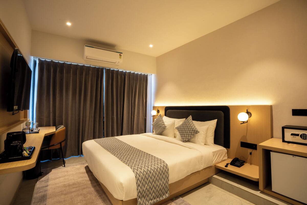 A hotel room with a bed, desk, chair, and a small desk with a phone and a lamp.