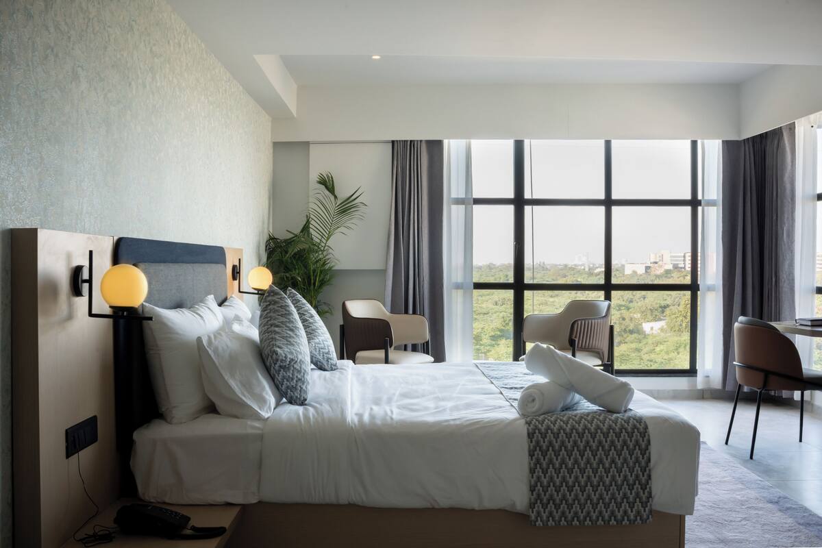 A modern hotel room with a large bed, a desk, and a view of the city.
