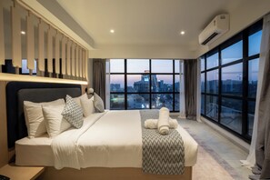 A modern hotel room with a large bed, a view of the cityscape, and an air conditioning unit. - Hotel Bellevue (Gandhinagar)