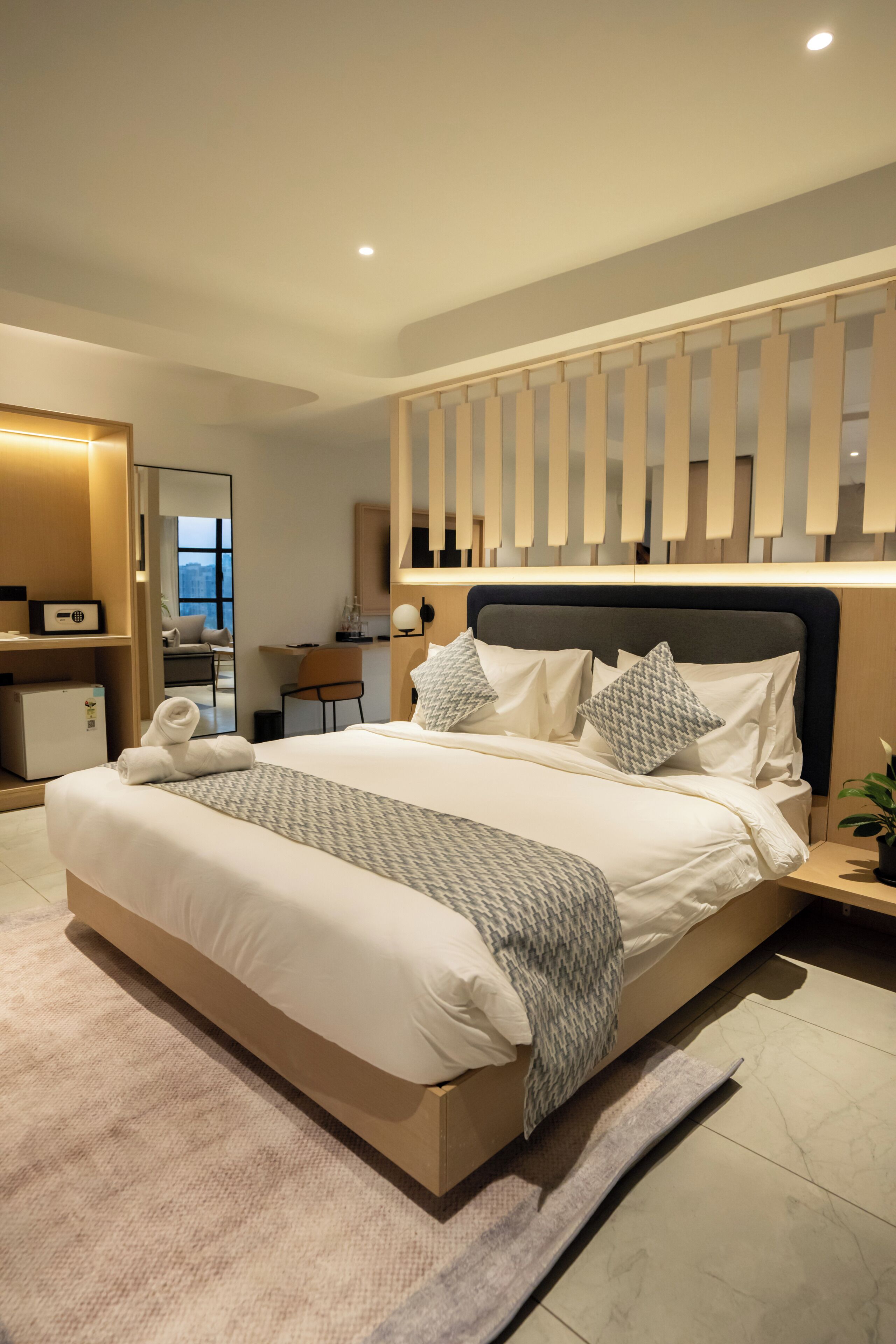 A modern hotel room with a large bed, a desk, and a view of the city.