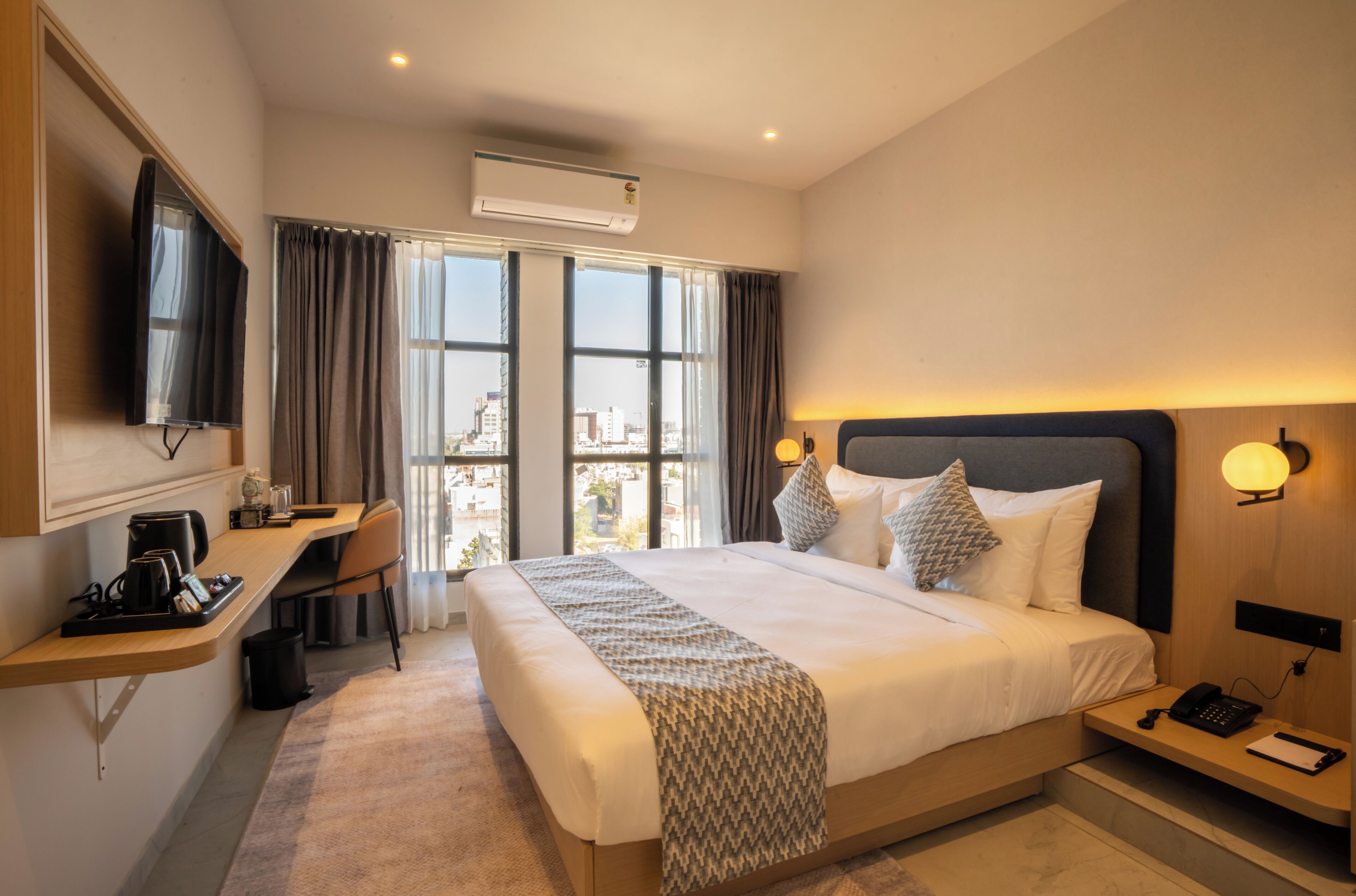 Une chambre d’hôtel avec un grand lit, un bureau avec un ordinateur, une télévision et une vue sur la ville.