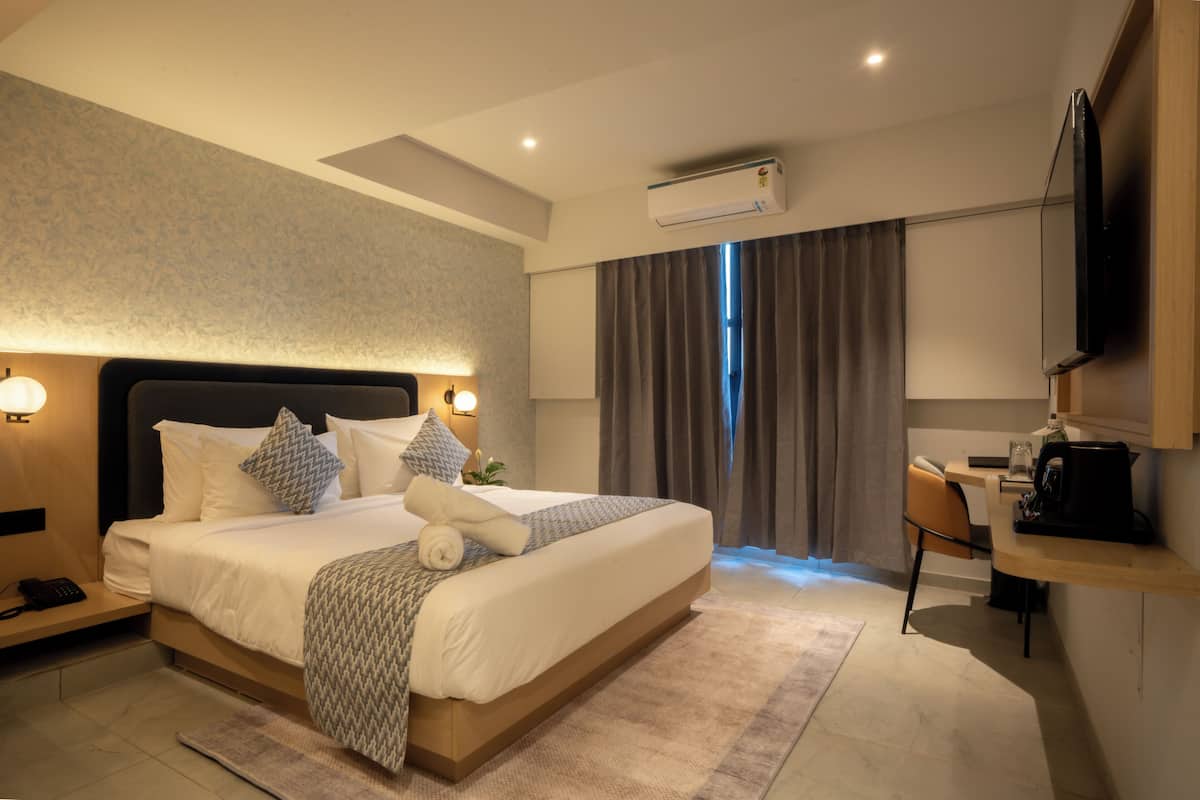 A modern hotel room with a large bed, bedside table, desk, and a flat-screen TV.