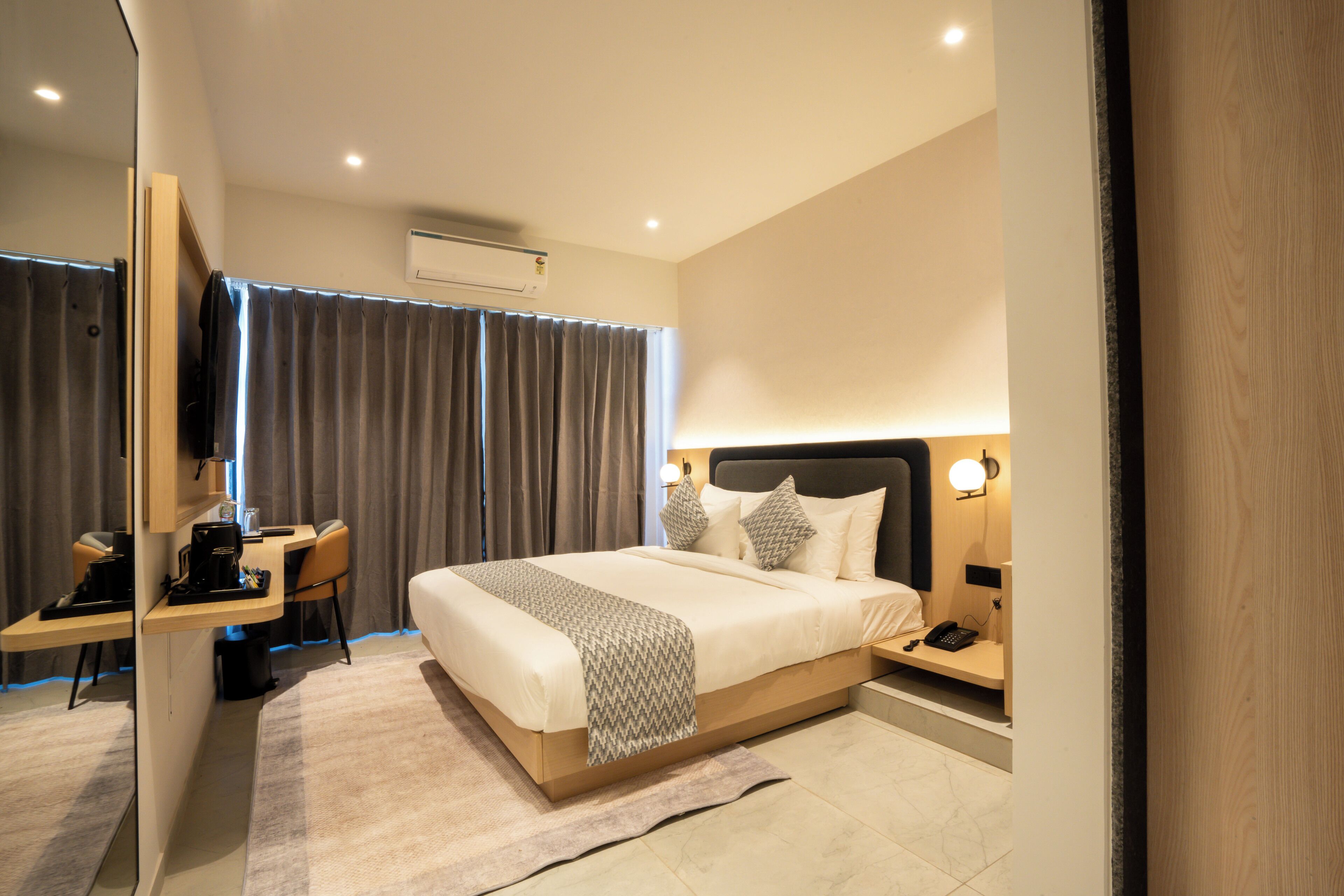 A modern hotel room with a large bed, bedside table, and a desk with a chair.