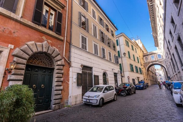 A narrow cobblestone street lined with historic buildings, parked cars, and a clear blue sky. - Domus Mondrian - Apartment in Central Roma (Roma)