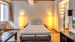 A bedroom with a bed, bedside lamps, a TV, and a window with curtains. - Domus Mondrian - Apartment in Central Roma (Roma)