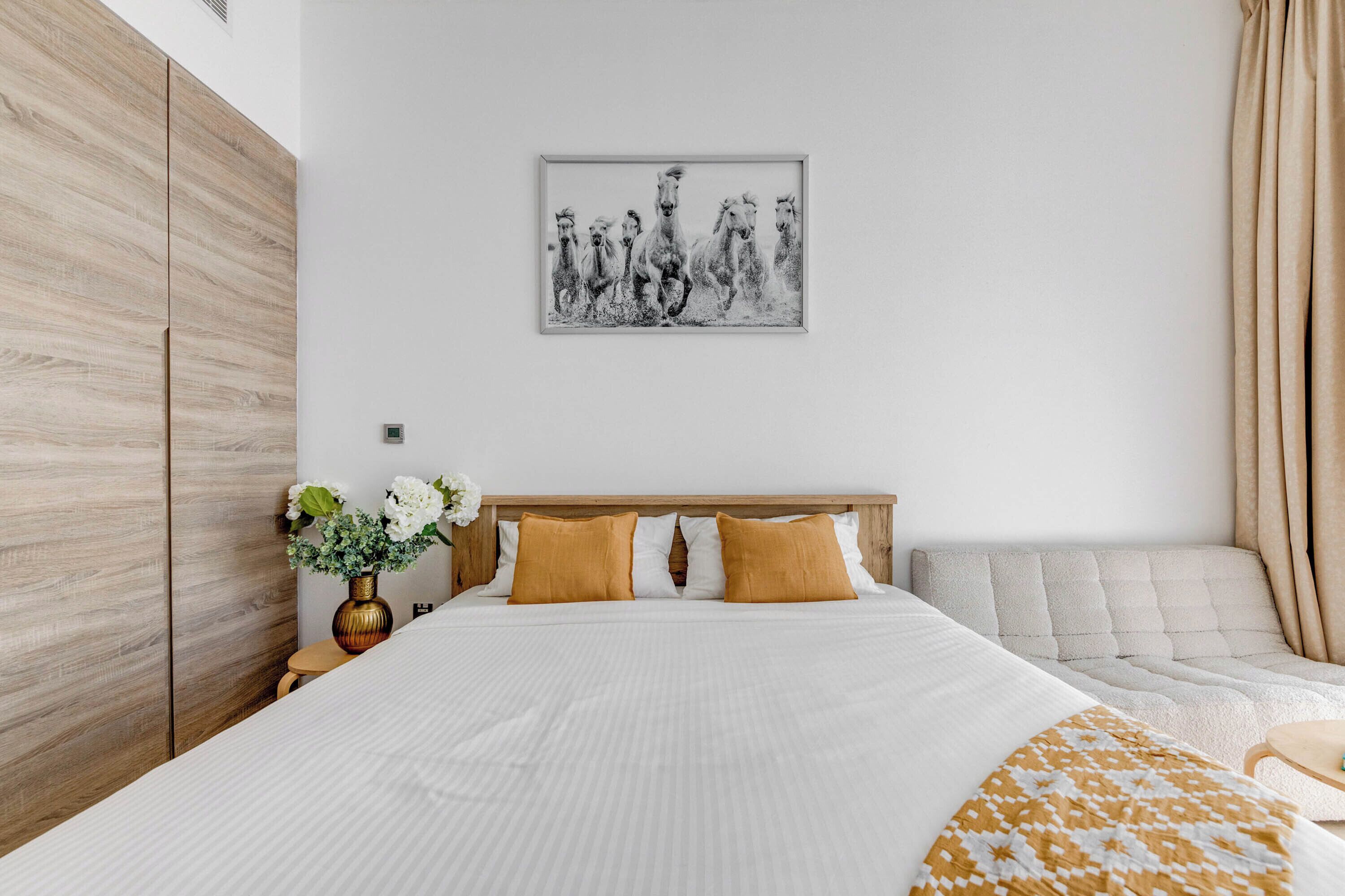 A bedroom with a large bed, a headboard, a bedside table with a vase, and a wall-mounted picture.