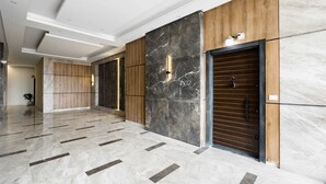 A spacious lobby with marble flooring, wooden paneling, and a modern elevator.