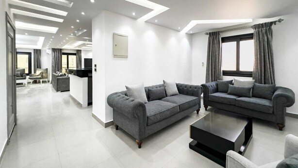 A modern living room with two grey sofas, a black coffee table, and a large window with curtains. - Xuru Stays I The Bold & Bright 3bdr Apt. 15 Min To Airport (Cairo)