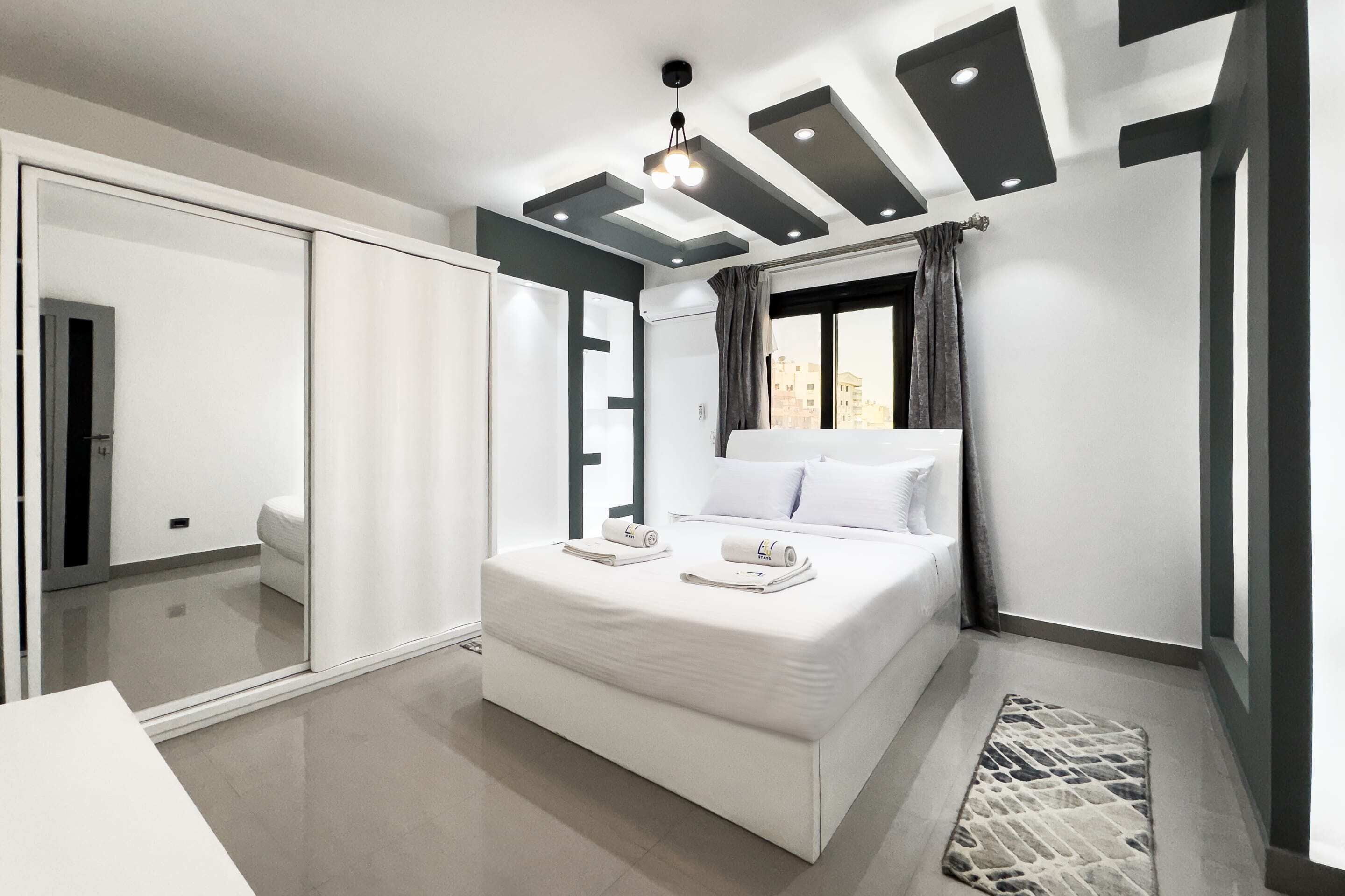 A modern bedroom with a large bed, a sliding door closet, and a view of the city through the window.