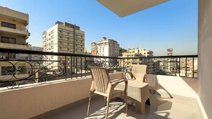 A balcony with a table and chairs, overlooking a cityscape with multiple buildings. - Xuru Stays I The Bold & Bright 3bdr Apt. 15 Min To Airport (Cairo)