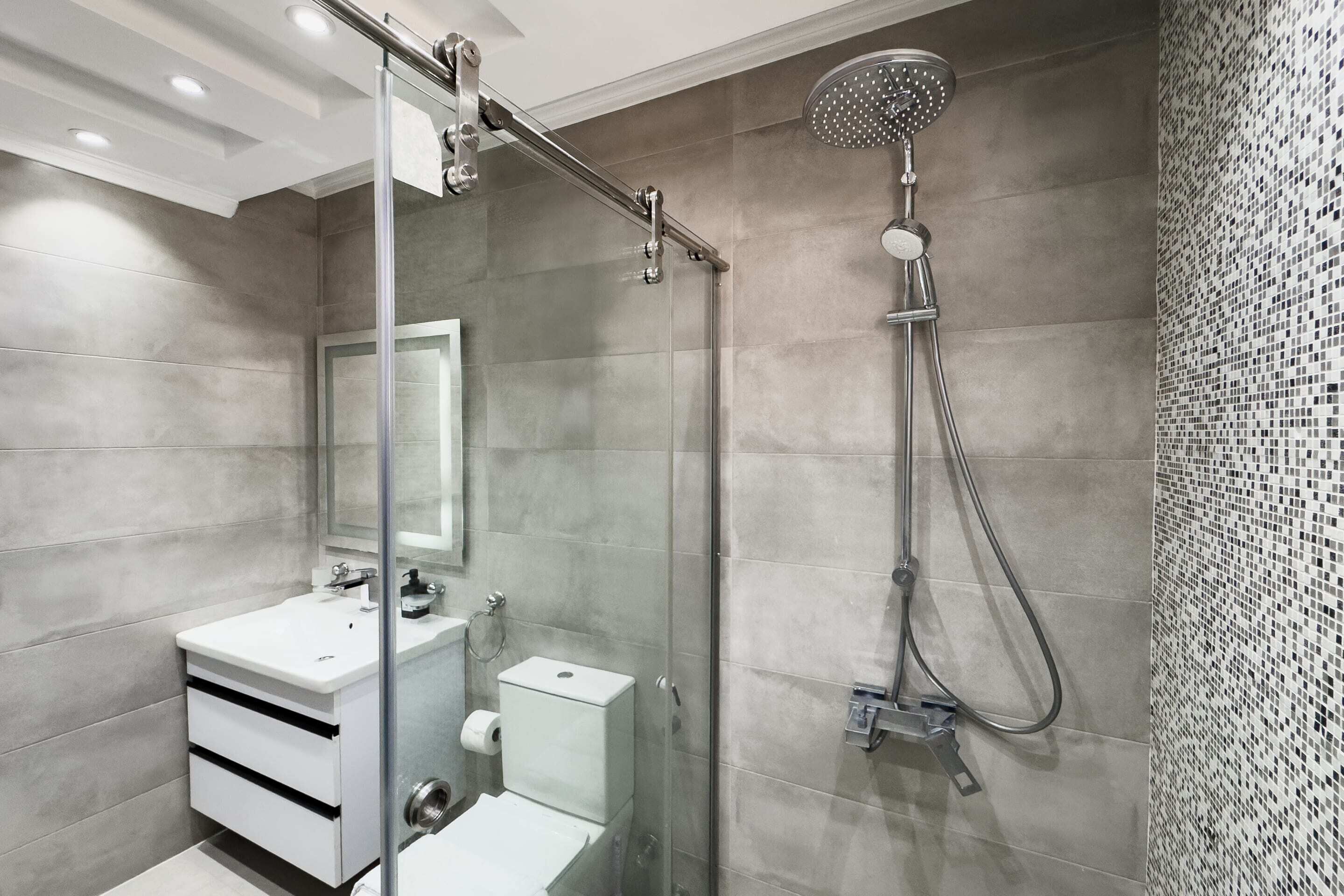 Une salle de bain moderne avec une douche à parois de verre, un lavabo blanc et une zone de douche carrelée.