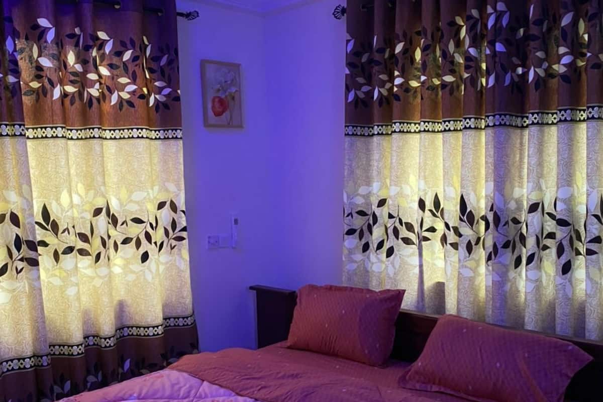 A bedroom with a bed, curtains with leaf patterns, a ceiling fan, and a wall-mounted light fixture.