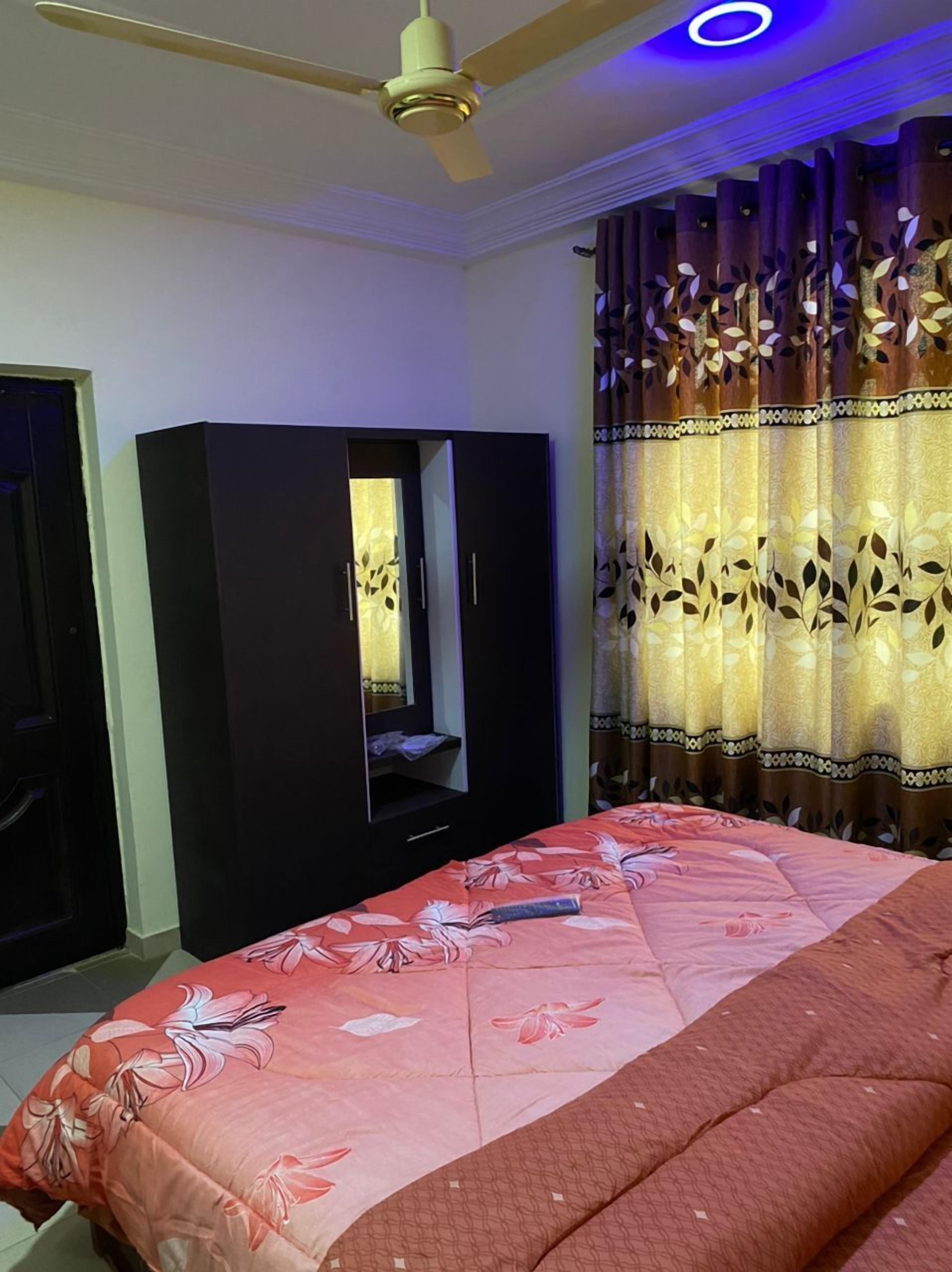 Une chambre à coucher avec un lit, une armoire, un ventilateur de plafond et des rideaux.