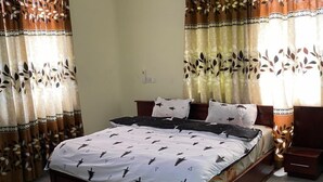 A bedroom with a bed, curtains, a ceiling fan, and a nightstand. - Ekoara Apartment (Sekondi-Takoradi)
