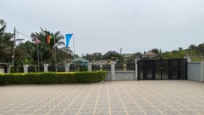 A spacious outdoor area with a patterned tile floor, a gated entrance, and a flagpole with multiple flags. - Ekoara Apartment (Sekondi-Takoradi)