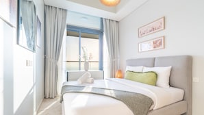 A modern bedroom with a large bed, a window with curtains, and two framed pictures on the wall.