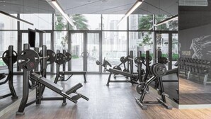 A modern gym with various weightlifting equipment, large windows, and a city view.