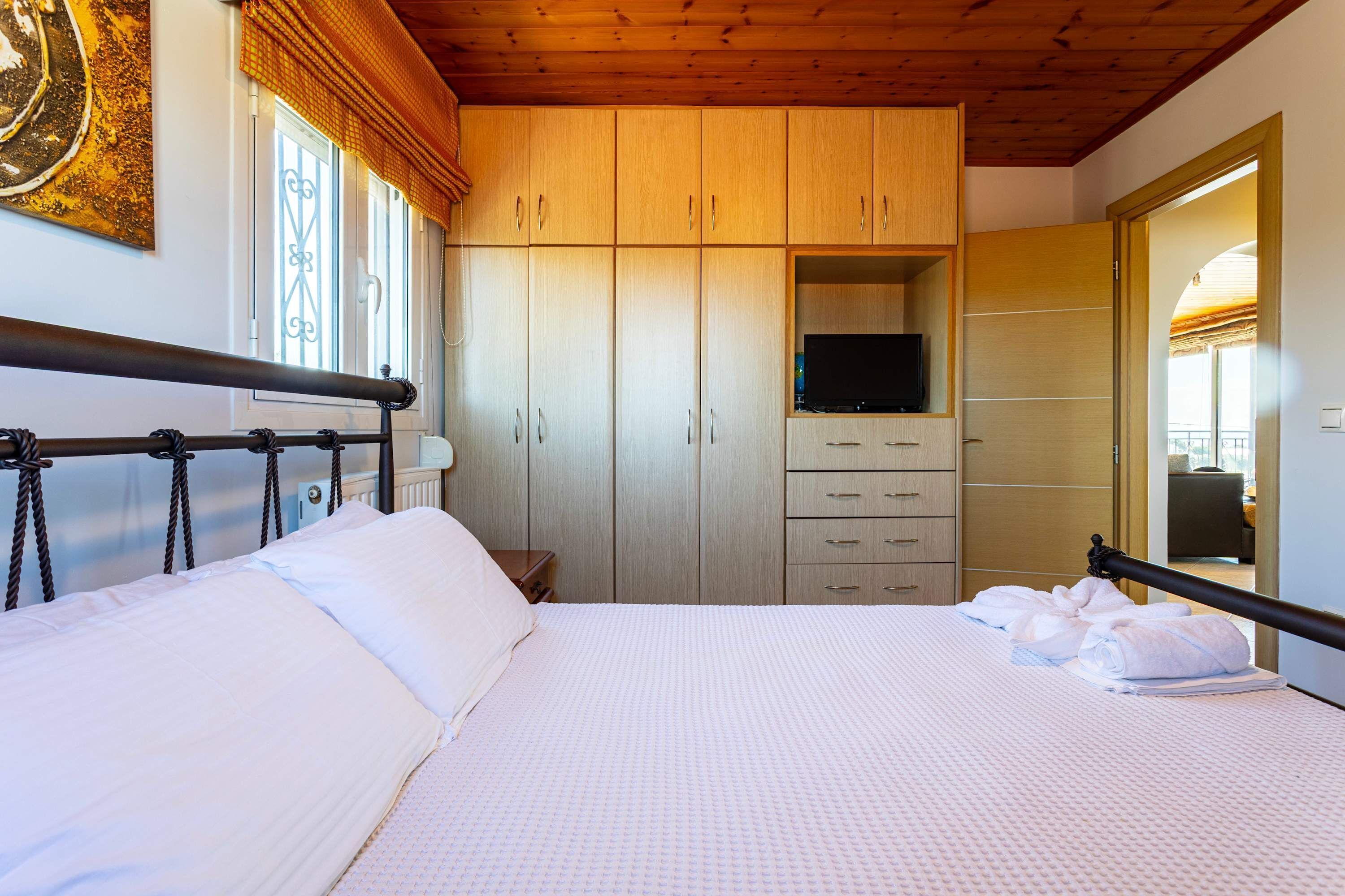 Un lit bien fait, avec du linge de lit blanc, un téléviseur posé sur un meuble et une armoire avec de nombreux tiroirs.