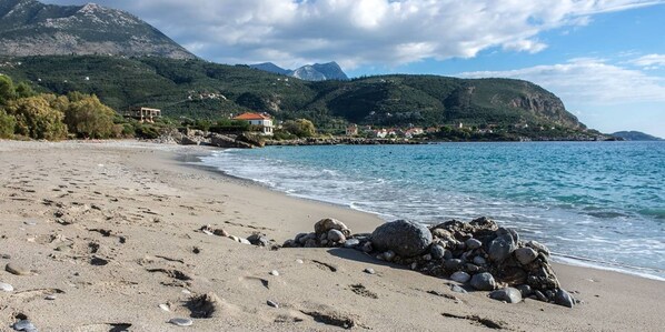 A beach with a rocky shoreline, a clear blue sea, and a mountainous backdrop.