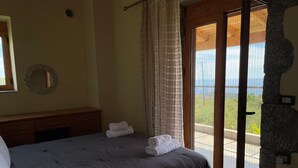 A bedroom with a bed, a nightstand, a mirror, and a view through a glass door to an outdoor area. - Stara Stone House Tranquil Garden Dazzling View (West Mani)