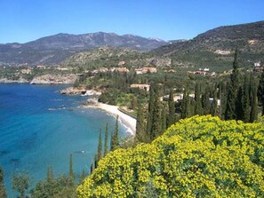 A coastal landscape with a clear view of the sea, a sandy beach, and a cluster of buildings on a hillside.