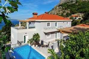A two-story house with a swimming pool, outdoor seating, and a view of the sea.