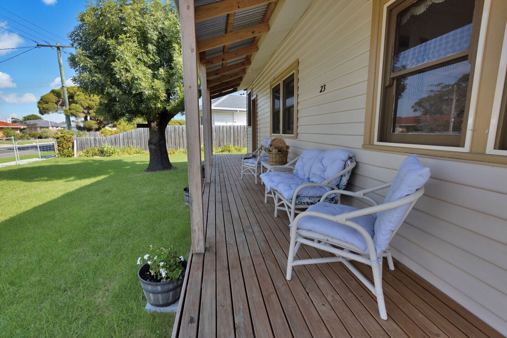 A wooden deck with two white wicker chairs and a table, a covered porch, and a well-maintained lawn.
