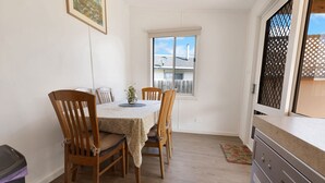 A dining area with a table set for four, wooden chairs, a vase with flowers, and a window with a view of a house.