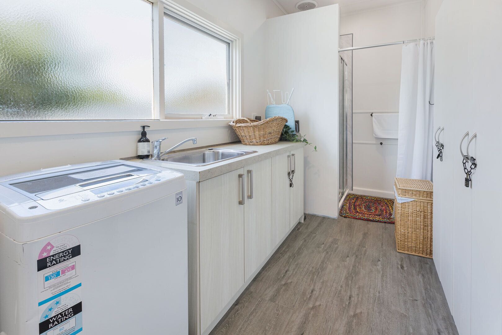 A compact kitchen with a washing machine, a sink, and a glass shower area.