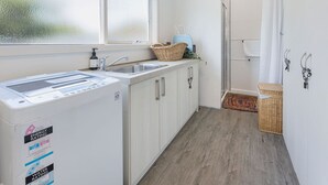 A compact kitchen with a washing machine, a sink, and a glass shower area.